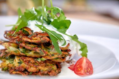 Ekşi kremalı kabak gözlemeleri ve beyaz tabakta bitkiler, yakın plan. 