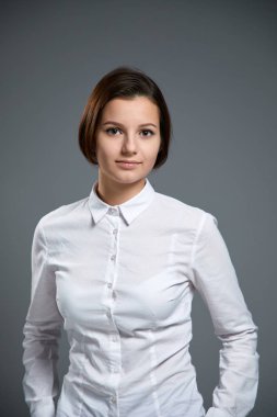 gri arka plan üzerinde poz beyaz gömlek giymiş güzel genç kadın portresi  