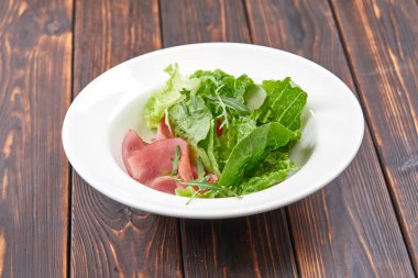 salad with lettuce and ham on white plate, close-up 