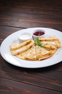 Beyaz tabakta ekşi kremalı ve çilek soslu krepler, yakın görüş.