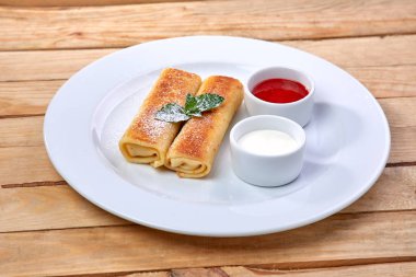 Beyaz tabakta ekşi kremalı ve çilek soslu krepler, yakın görüş.