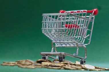 Yeşil arka planda alışveriş sepetinin altında madeni paralar