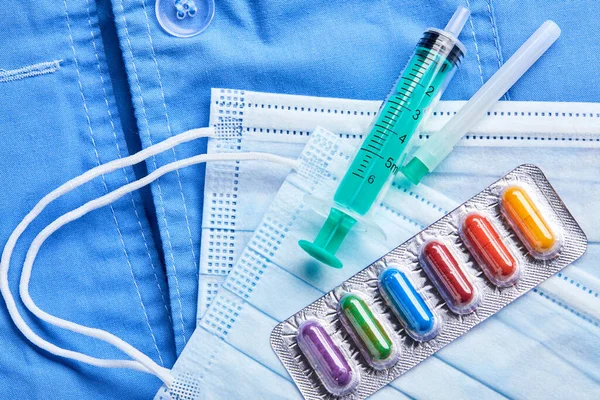 Pharmaceutical medicine syringe and medical mask with capsules on blue background. Medicine concept. Coronavirus