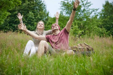 güneşli bir günde ormana yakın çayırda oturan iki gezgin 