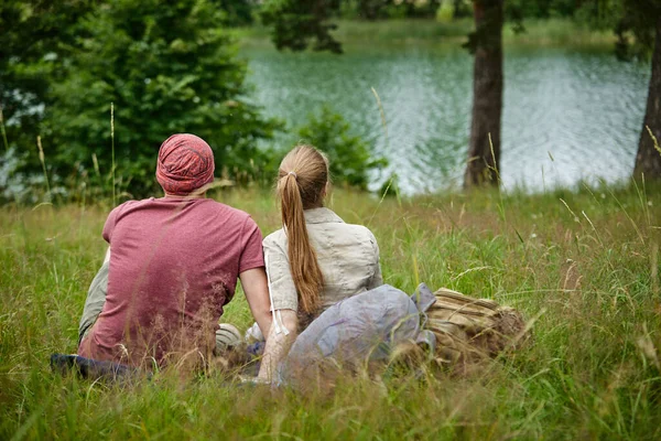 阳光明媚的日子 两个旅行者坐在湖边的草地上 — 图库照片