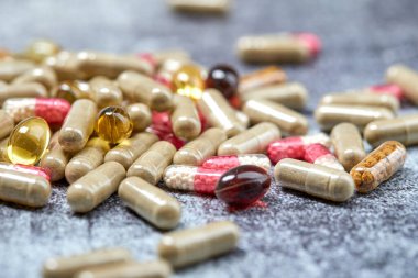 Gri yüzeyde ilaç hapları ve kapsüller yığını