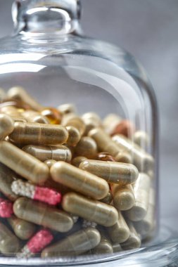 İlaç hapları ve kapsüller gri yüzeydeki cam örtülerin altında.