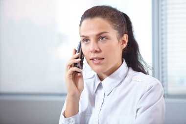 İş kadını ofiste otururken telefonla konuşuyor.