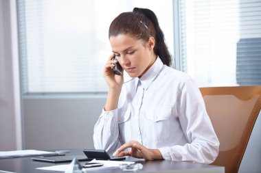 İş kadını ofiste otururken telefonla konuşuyor.
