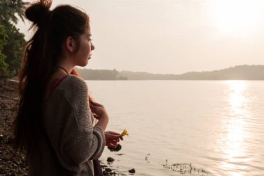 Asyalı kız elinde çiçekle sahilde duruyor, gün batımıyla karşılaşıyor.