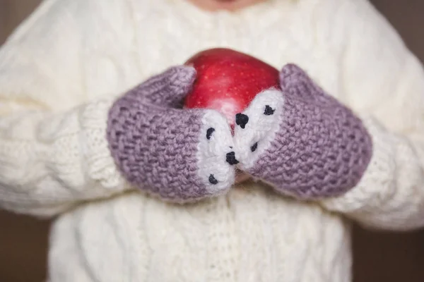 Manos de los niños en manoplas acogedoras sosteniendo manzana roja — Foto de Stock