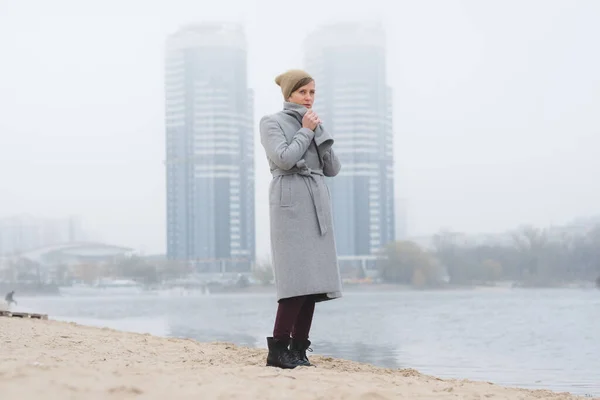 Young woman walking away alone wearing a grey overcoat