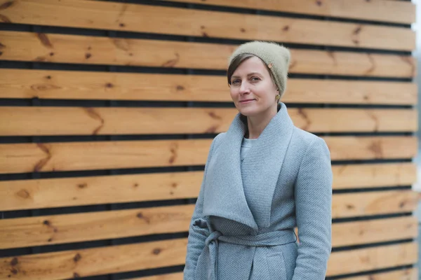 Jonge vrouw in een grijze overjas, houten achtergrond — Stockfoto