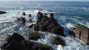Büyük dalgalar Tenerife Adası 'ndaki siyah volkanik kayalara çarpıyor. Derin mavi bir okyanusun sinematik çekimi kayalık kıyılarda şiddetli bir şekilde dalgalanır.
