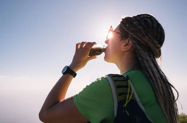 Portrait d'une jeune femme buvant de l'eau d'une bouteille en s'asseyant et se reposant après avoir couru le sentier — Photo