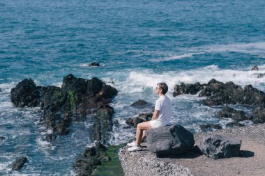 Denize bakan bankta oturan genç bir kadın. Tenerife Adası, İspanya