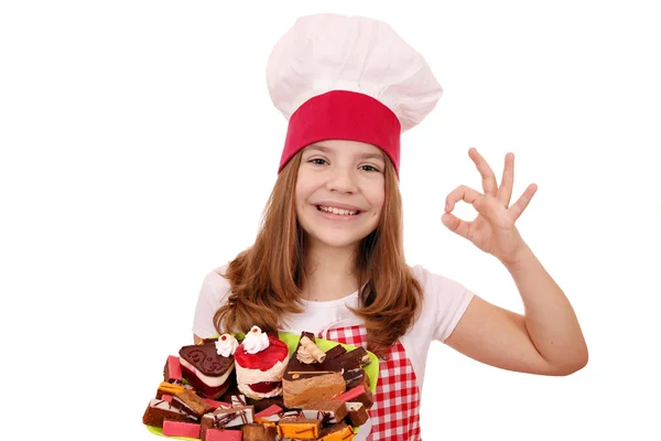 Feliz niña cocinero con dulces pasteles y signo de mano — Foto de Stock