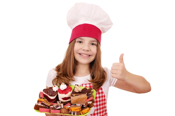 Feliz niña cocinero con dulces pasteles y pulgar hacia arriba —  Fotos de Stock