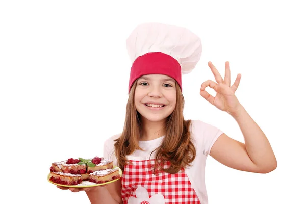 Mutlu küçük kız yemek ev yapımı kek ve ok el işareti ile — Stok fotoğraf