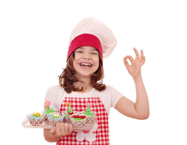 Lycklig liten flicka koka med muffin och ok hand tecken — Stockfoto