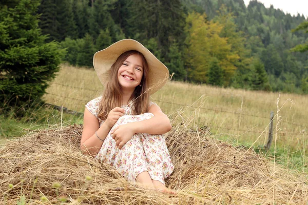 Boldog kis lány ül a széna vidéki nyári szezonban — Stock Fotó