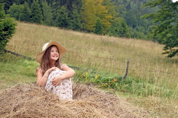 Glückliches kleines Mädchen auf Heu sitzend — Stockfoto