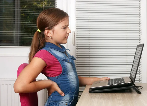 Niña tiene dolor de espalda mientras usa una computadora portátil — Foto de Stock