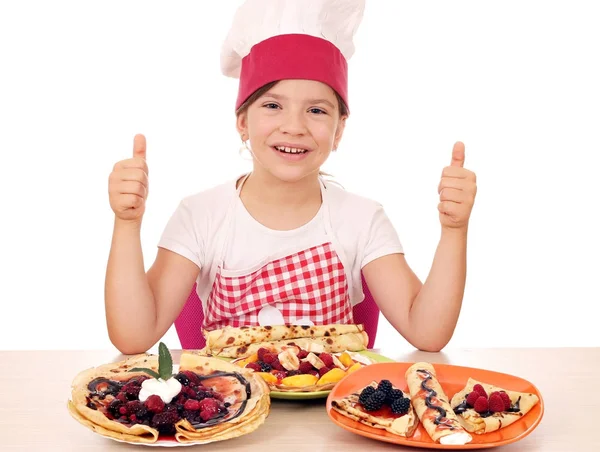 Happy little girl cook with crepes and thumbs up — Stock Photo, Image