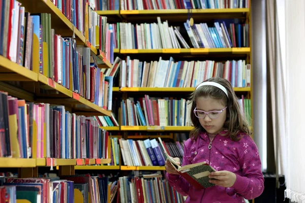 Krásná holčička, čtení knihy v knihovně — Stock fotografie