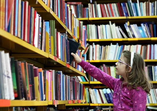 Liten flicka tar en bok på biblioteket — Stockfoto