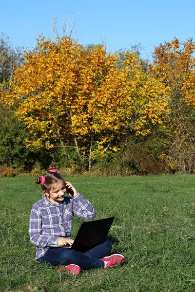 Kleines Mädchen spielt Laptop und spricht auf Smartphone — Stockfoto
