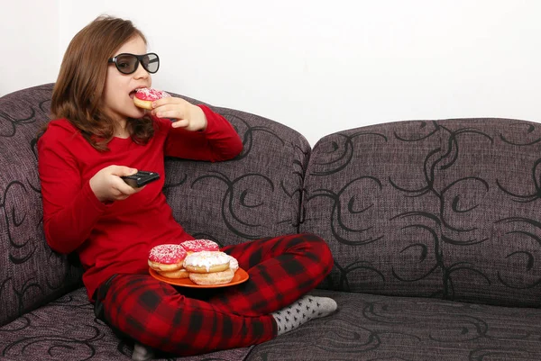 Happy little girl watching 3d tv and eating donuts — Stock Photo, Image