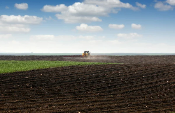 Tractor spraying plowed field at spring — Stock Photo, Image