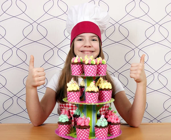 Счастливая маленькая девочка готовит с кексами и большими пальцами вверх — стоковое фото