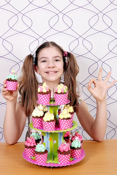 Šťastná holčička s muffiny moučníky a značka ok ruky — Stock fotografie