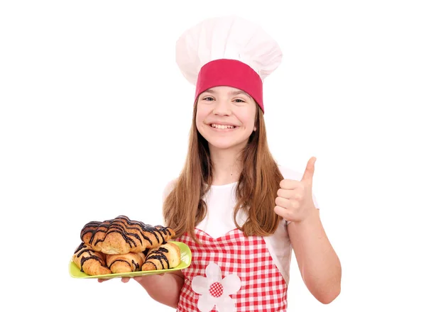 Happy little girl cook with croissant and thumb up — Stock Photo, Image