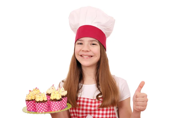 Feliz niña cocinera con magdalenas y el pulgar hacia arriba — Foto de Stock