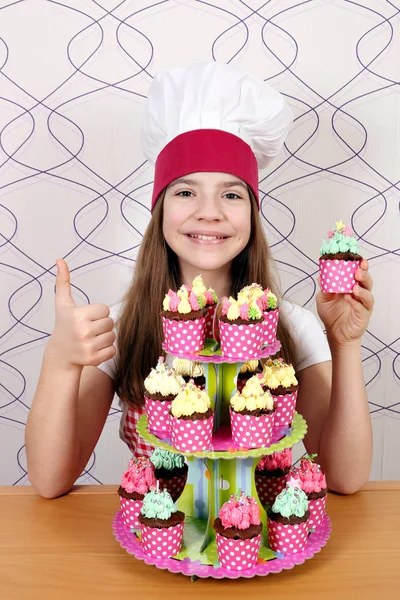 Happy little girl cook with sweet muffins dessert and thumb up