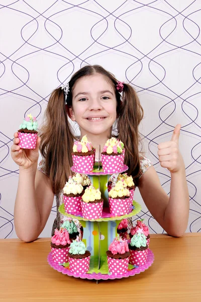 Menina feliz cozinhar com muffins e polegar para cima — Fotografia de Stock