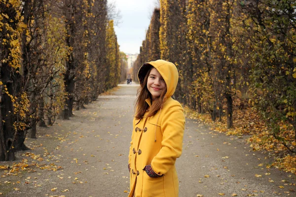 Chica feliz en un abrigo con capucha amarilla en el parque Augarten Viena a — Foto de Stock