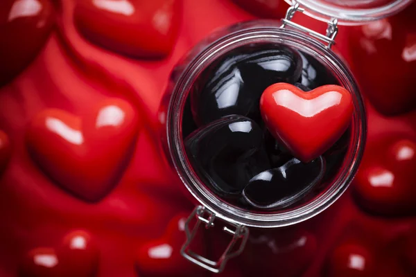 Frasco de vidro cheio de corações pretos e coração vermelho em cima e vermelho para trás — Fotografia de Stock