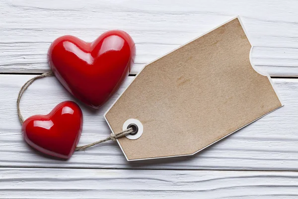 Dois corações vermelhos e uma etiqueta de papel na mesa de madeira — Fotografia de Stock