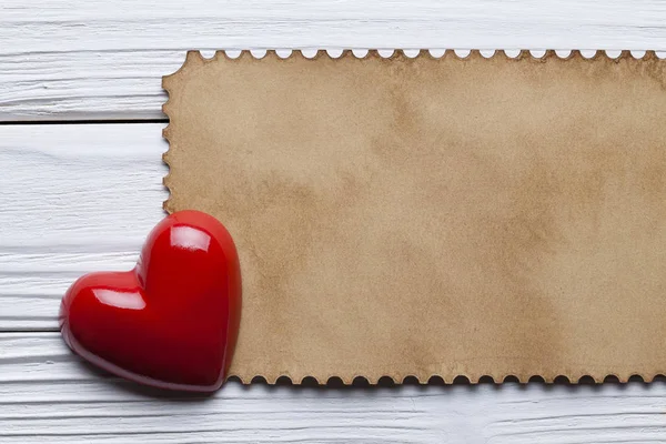 Um coração vermelho e folha de papel em branco na mesa de madeira — Fotografia de Stock