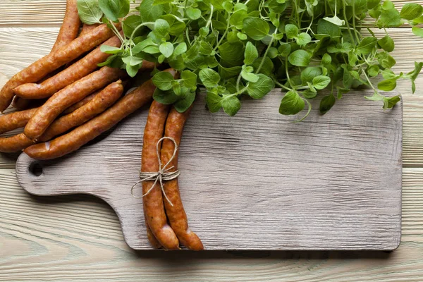 Сырая колбаса, доска для резки и свежие травы на деревянном столе — стоковое фото