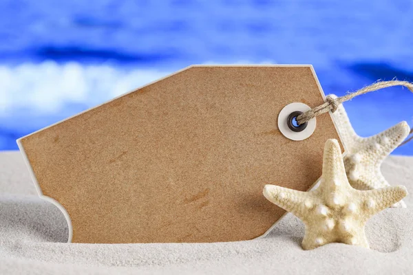 Üres papír címke és tengeri csillag a tengerparti homok és a tenger a háttérben — Stock Fotó