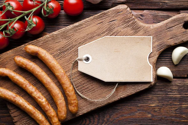 Простая бумажная этикетка, сырая колбаса и овощи на деревянном столе — стоковое фото