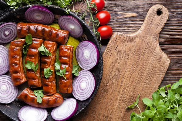 Жареная колбаса в кастрюле, резка доски и свежие овощи на — стоковое фото
