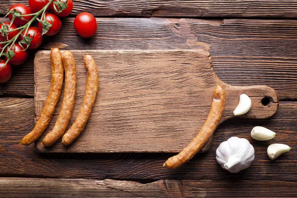 Сырая колбаса, помидоры и чеснок на деревянном столе — стоковое фото