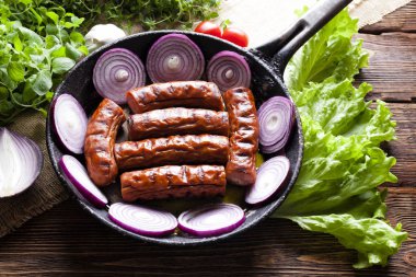 Bir tava ve ahşap masa üzerinde taze sebze ızgara sosis