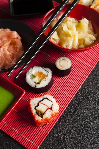 Rolos de sushi, gengibre e wasabi em tapete vermelho e mesa preta — Fotografia de Stock